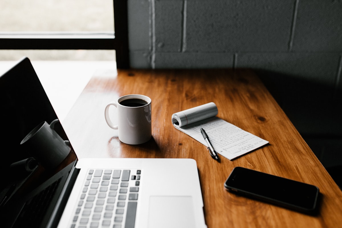 Un ordinateur portable, un café et un carnet de notes sur un bureau en bois