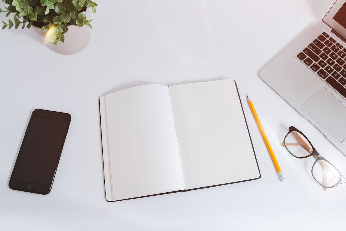 Un bureau épuré avec un carnet, un téléphone, des lunettes et un ordinateur portable