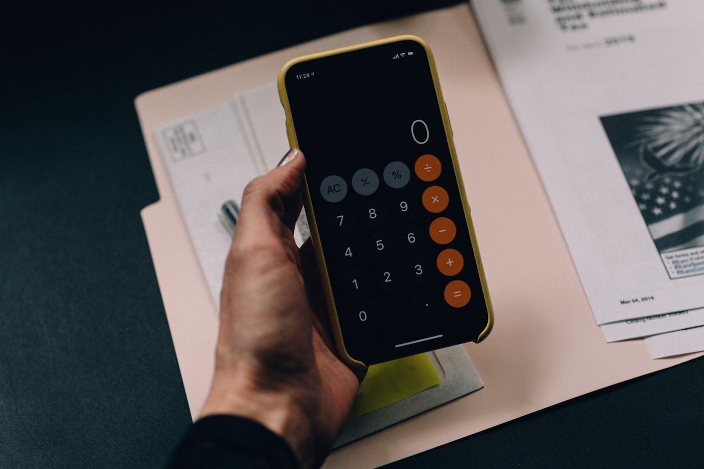 Une main tenant un téléphone affichant une calculatrice posée sur des documents